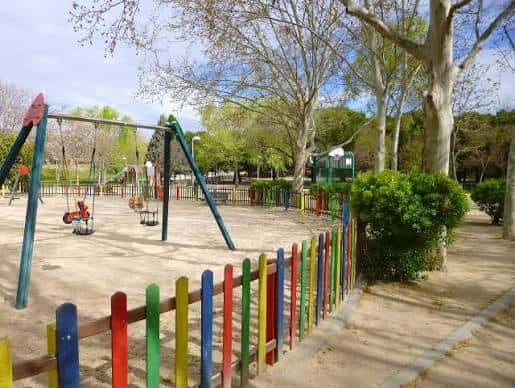 Zona de juegos infantiles con columpios y valla colorida en el Parque Norte