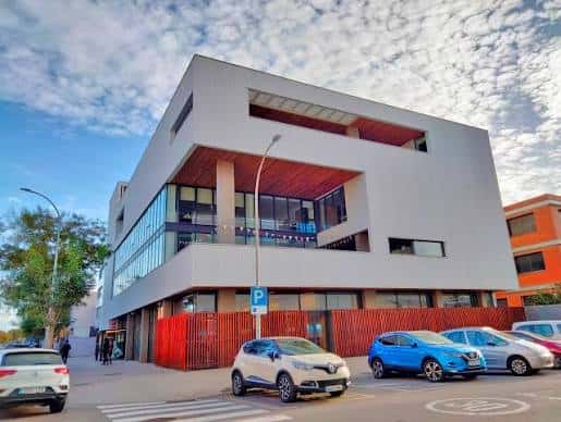 Fachada principal del centro con cielo azul y vehículos estacionados frente al edificio