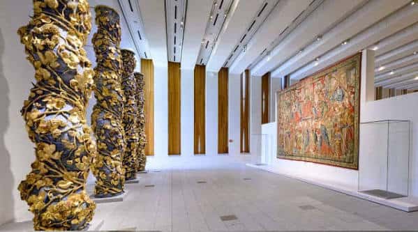 Vista de columnas ornamentadas doradas y gran tapiz en la galería