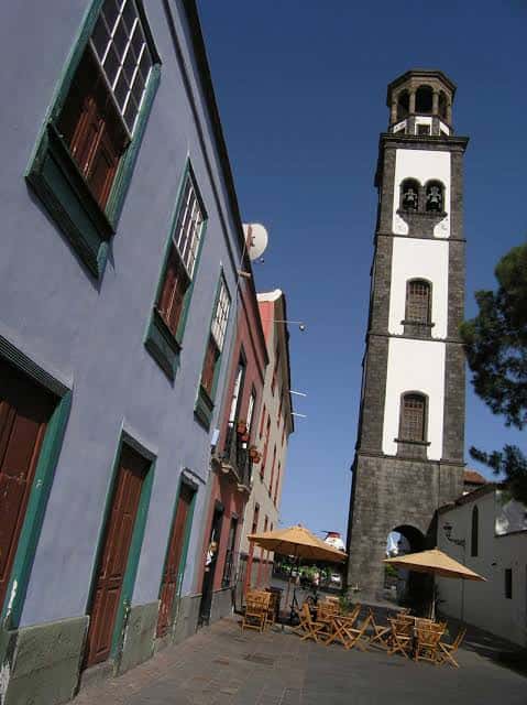Vista lateral de la plaza con la torre de la iglesia y mesas de terraza en primer plano