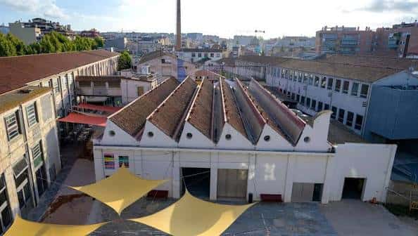 Vista aérea de la fachada principal de Roca Umbert con sus característicos tejados a dos aguas y toldos amarillos en el patio