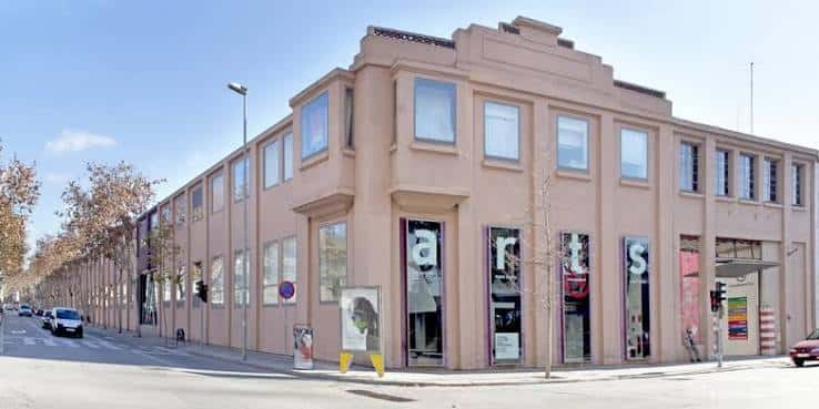 Fachada lateral del edificio Roca Umbert con grandes ventanales y la palabra 'arts' visible en los cristales