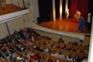 Interior del auditorio de Sa Societat durante una representación teatral, con público sentado y actores en el escenario