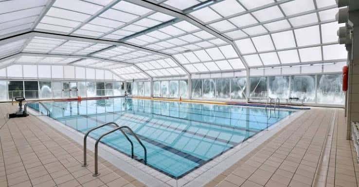 Piscina cubierta del complejo deportivo con estructura de cristal y techo translúcido