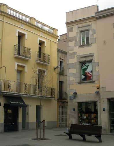 Vista de la fachada amarilla con balcones y la esquina de piedra de la Plaça de les Olles