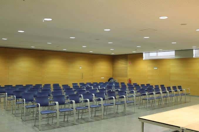Sala de actos interior con sillas azules dispuestas para un evento y paredes de madera clara