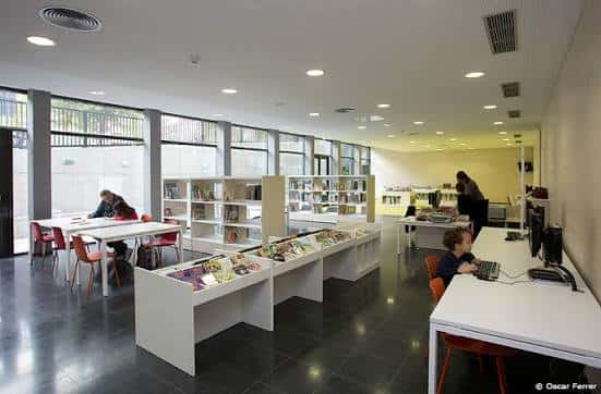 Interior luminoso de la biblioteca con mesas de lectura y estanterías blancas