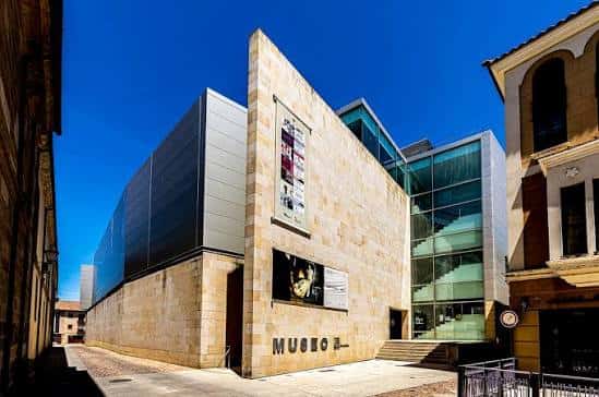 Vista frontal del museo con cartel de exposición y escalera de cristal