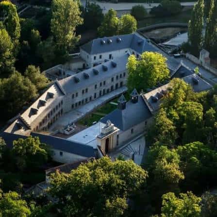Vista aérea del complejo de la Real Casa de la Moneda en Segovia, mostrando sus edificios históricos rodeados de vegetación