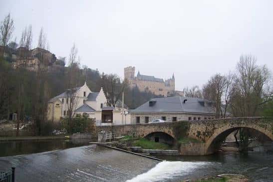 Panorámica de la Real Casa de la Moneda con el Alcázar de Segovia al fondo, capturando la integración del edificio en el paisaje urbano