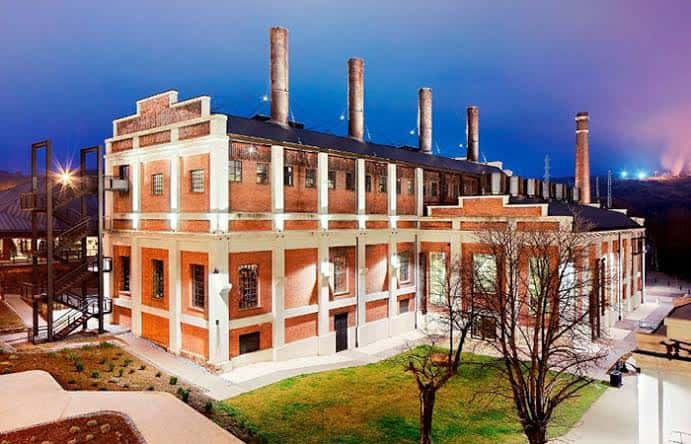 Vista nocturna del Museo de la Energía con fachada iluminada y chimeneas industriales