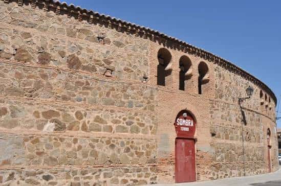 Fachada exterior de la Plaza de Toros de Toledo con mampostería de piedra y puerta roja marcada como 'SOMBRA'