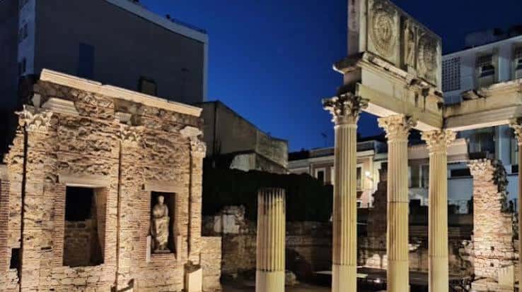 Iluminación nocturna del Pórtico del Foro Municipal, destacando las columnas y relieves bajo cielo azul oscuro