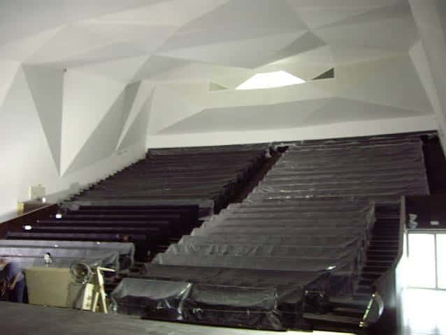 Interior del auditorio con butacas cubiertas y techo de diseño geométrico blanco