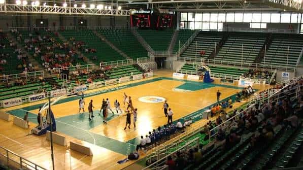 Interior del pabellón durante un partido de baloncesto con gradas verdes y pista de madera