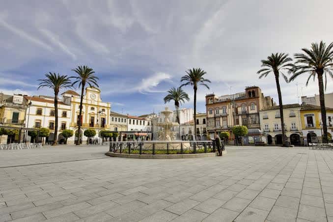 Plaza de España con fuente central y palmeras bajo cielo parcialmente nublado