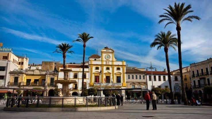 Fachada amarilla del ayuntamiento en la plaza con palmeras y cielo azul intenso