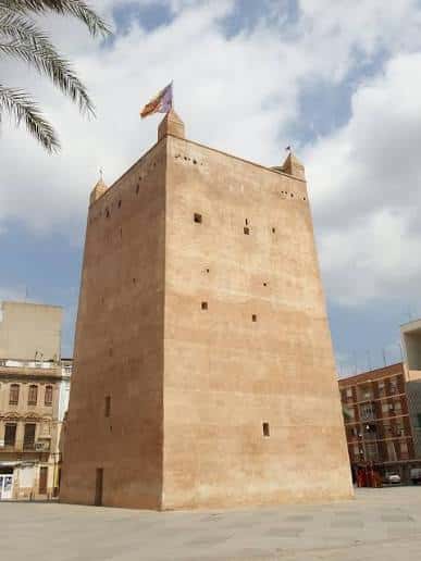 Vista frontal de la Torre de Torrente en la Plaza Mayor, con bandera y cielo parcialmente nublado