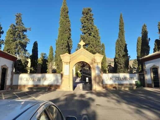 Entrada principal del Cementerio de San Clemente con arco decorado y cipreses altos bajo cielo azul