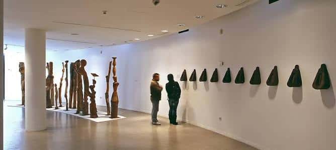 Interior de la galería de arte con esculturas y visitantes observando las obras