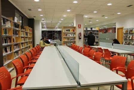 Interior de la sala de lectura con mesas blancas y sillas naranjas