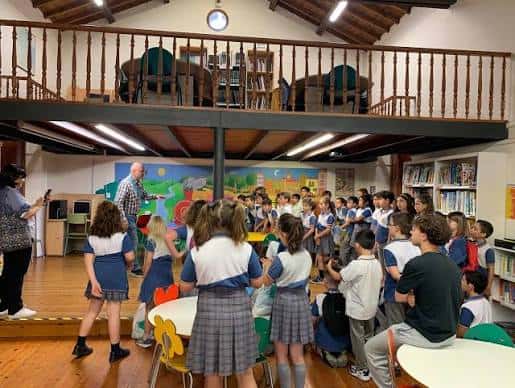 Interior de la biblioteca con grupo escolar en evento, mostrando mezzanine y zona infantil decorada