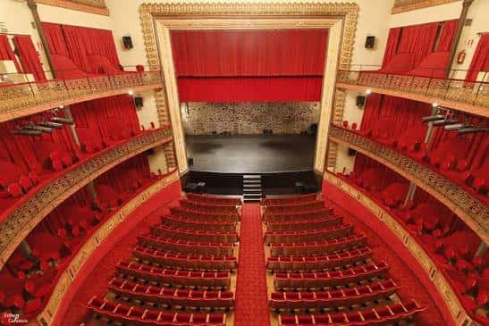 Vista frontal del auditorio con el telón rojo cerrado y el escenario