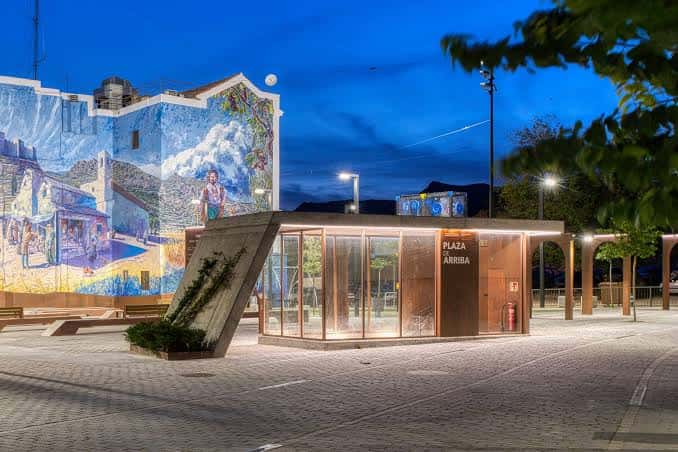 Plaza de Arriba al atardecer, mostrando el mural iluminado y la estructura de vidrio con señalización