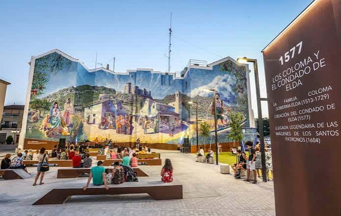 Plaza de Arriba con visitantes disfrutando del espacio público frente al mural y panel informativo histórico