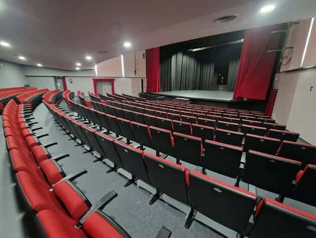 Interior del auditorio con butacas rojas y escenario con cortinas rojas