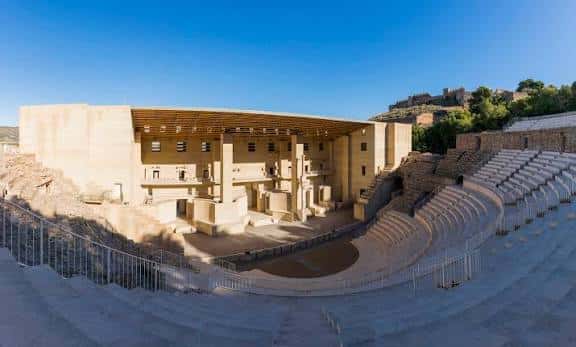 Vista panorámica del Teatro Romano de Sagunto con el escenario moderno y las gradas antiguas bajo un cielo despejado