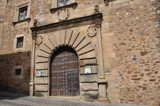 Vista exterior de la fachada principal del Palacio de Godoy con su imponente puerta de arco de medio punto y detalles arquitectónicos en piedra