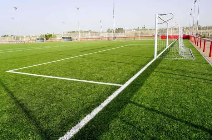 Campo de fútbol con césped artificial, líneas blancas y portería en primer plano