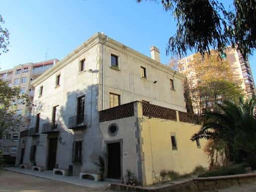 Fachada principal de Les Esmandies, un edificio histórico de piedra con balcones y entorno arbolado