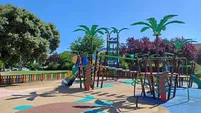 Área de juegos infantiles con palmeras artificiales y columpios en Parque Primero de Mayo