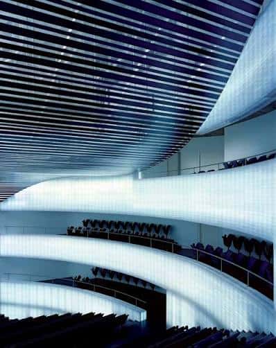 Interior del auditorio con techo ondulado y balcones curvos iluminados