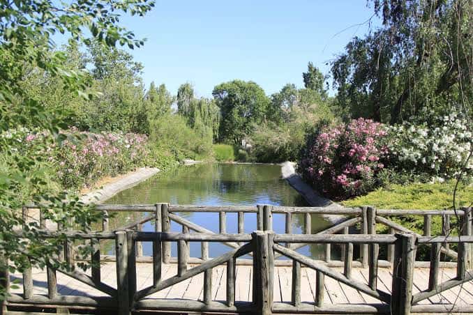 Paisaje natural del parque con puente de madera, río y jardines floridos