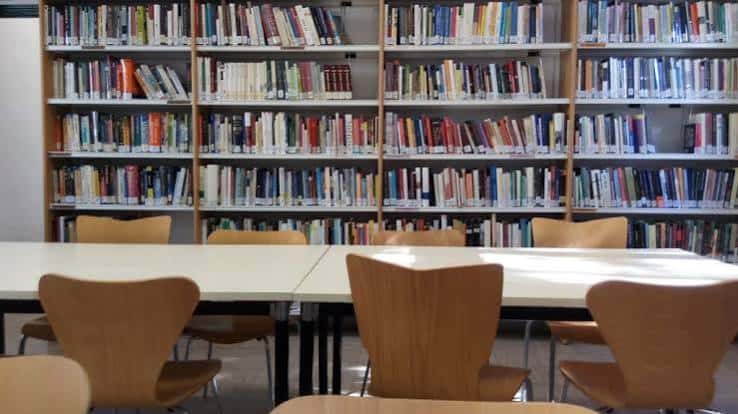 Interior de la biblioteca con estanterías llenas de libros y mesas de lectura con sillas de madera