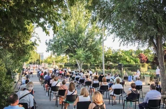 Evento al aire libre en el parque con asistentes sentados bajo árboles