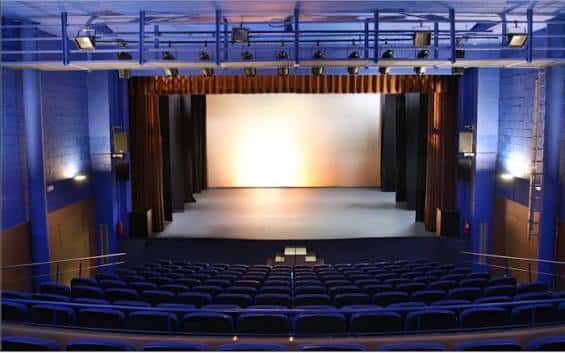 Interior del auditorio con escenario, cortinas y butacas azules