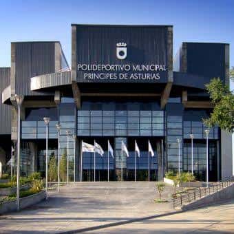 Fachada principal del polideportivo con banderas y acceso peatonal en día soleado