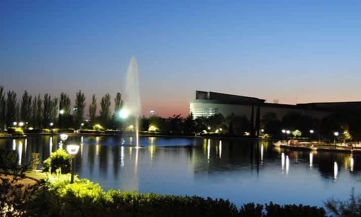 Vista nocturna del lago con fuente iluminada y edificio moderno al fondo