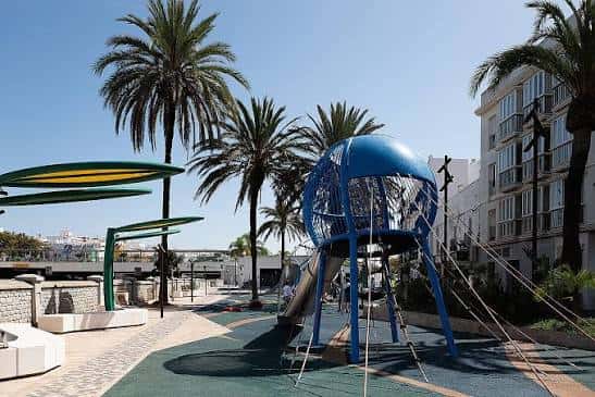 Área de juegos infantiles junto al Anfiteatro, con palmeras y estructura azul en primer plano