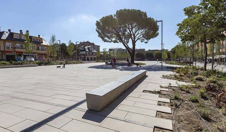 Plaza de los Belgas con bancos de hormigón y personas paseando, mostrando el espacio público en uso