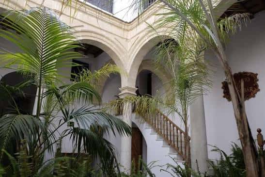 Patio interior del palacio con arcos, escalera y vegetación tropical