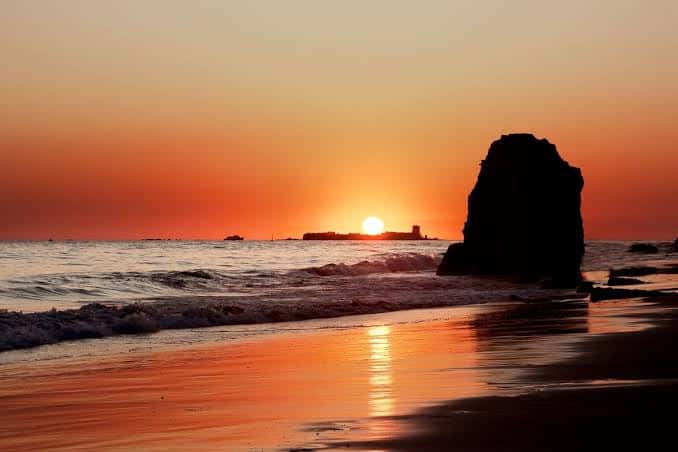 Atardecer en la Playa de la Barrosa con silueta de roca y castillo al fondo