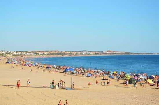 Playa de la Barrosa concurrida en un día soleado con el mar azul