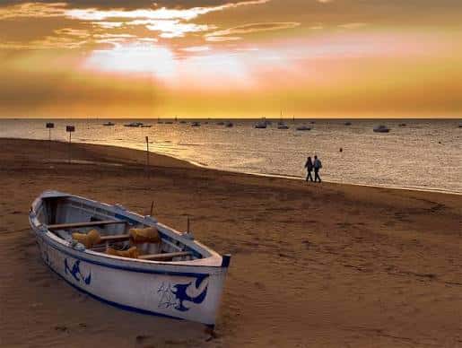 Atardecer romántico en la playa con una barca tradicional y parejas caminando