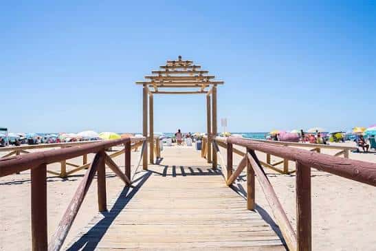 Pasarela de madera que conduce a la playa con sombrillas y cielo despejado