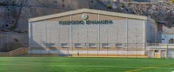 Vista exterior del Polideportivo Municipal Ramón Rico durante el día, con fachada clara y campo de césped artificial